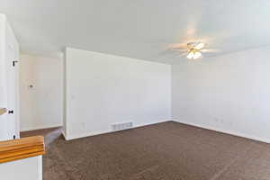 Unfurnished room featuring dark colored carpet, a ceiling fan, and a textured ceiling