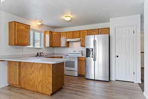 Kitchen featuring stainless steel fridge, light countertops, a peninsula, white electric stove, and brown cabinetry