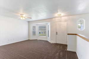 Spare room with a textured ceiling, plenty of natural light, dark colored carpet, and a ceiling fan