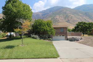 Obstructed view of property with a mountain view, concrete driveway, a garage, brick siding, and a front yard
