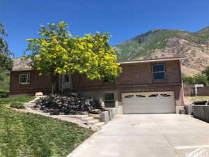 View of front of home featuring brick siding, a mountain view, concrete driveway, an attached garage, and a front yard