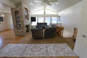Living area with ceiling fan, lofted ceiling, a fireplace, and wood finished floors