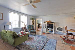 Living area featuring light tile patterned flooring, a ceiling fan, heating unit, and brick wall