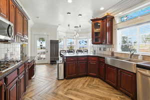 Kitchen with backsplash, hanging light fixtures, stainless steel appliances, ornamental molding, and dark cherry cabinets