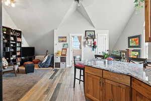 Kitchen with a breakfast bar, brown cabinetry, lofted ceiling, a ceiling fan, and light wood-type flooring