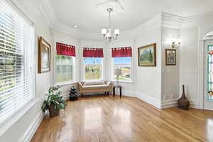 Sitting room with ornamental molding, light wood-type flooring, healthy amount of natural light, and a chandelier