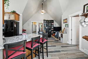 Kitchen featuring light stone countertops, freestanding refrigerator, a breakfast bar, light wood-style flooring, and vaulted ceiling