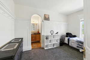 Bedroom with dark colored carpet, arched walkways, and ensuite bath