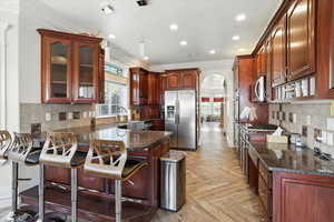 Kitchen featuring backsplash, arched walkways, stainless steel appliances, recessed lighting, and ornamental molding