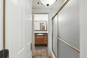 Bathroom featuring vanity, dark stone finish flooring, crown molding, and shower / bath combination with glass door