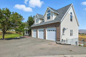 View of side of property featuring brick siding, asphalt driveway, roof with shingles, and an attached garage