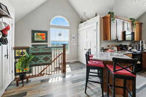 Kitchen featuring a kitchen breakfast bar, light wood-style floors, black appliances, light stone counters, and high vaulted ceiling