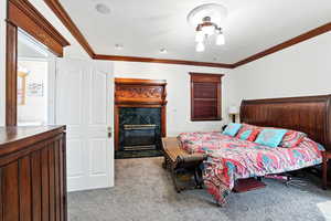 Bedroom featuring ornamental molding, a custom fireplace, and carpet floors