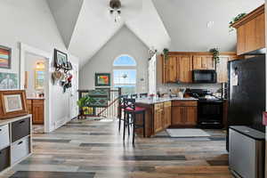 Kitchen featuring brown cabinets, a breakfast bar, black appliances, light wood finished floors, and a peninsula