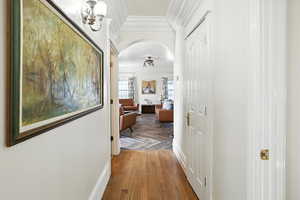 Hallway featuring arched walkways, light wood-style floors, and ornamental molding
