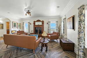Living room featuring a fireplace, healthy amount of natural light, ornamental molding, arched walkways, and a textured ceiling