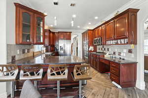 Kitchen featuring arched walkways, backsplash, ornamental molding, a peninsula, and dark stone counters