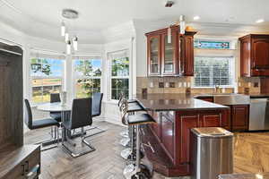 Kitchen featuring pendant lighting, ornamental molding, decorative backsplash, dark stone counters, and dishwasher