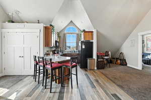 Dining space with vaulted ceiling, light wood-style floors, and light carpet