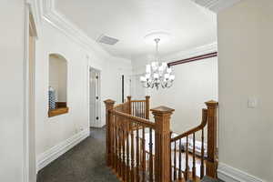 Hallway with an upstairs landing, crown molding, a chandelier, and dark carpet