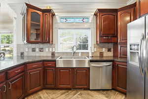 Kitchen featuring appliances with stainless steel finishes, ornamental molding, tasteful backsplash, glass insert cabinets, and dark cherry cabinets