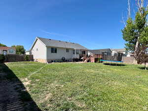 Rear view of property featuring a trampoline, a fenced backyard, a wooden deck, a patio, and stairway