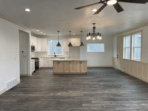 Kitchen with ornamental molding, stainless steel appliances, decorative light fixtures, a kitchen island, and dark wood-type flooring