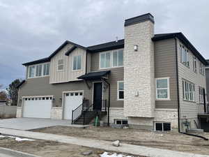View of front of home with a garage, stone siding, concrete driveway, a chimney, and board and batten siding