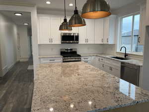 Kitchen with white cabinets, stainless steel appliances, dark wood finished floors, recessed lighting, and light stone countertops