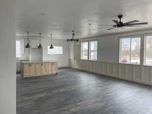 Unfurnished living room featuring dark wood-style floors, a textured ceiling, a ceiling fan, crown molding, and a chandelier