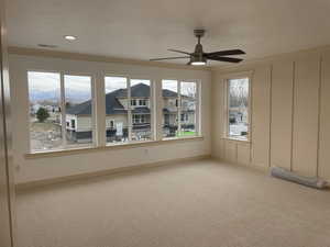 Unfurnished room featuring carpet, plenty of natural light, and ceiling fan