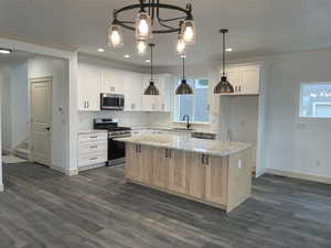 Kitchen with a kitchen island, stainless steel appliances, light stone counters, hanging light fixtures, and white cabinetry