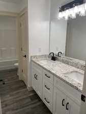 Full bathroom with double vanity, dark wood-type flooring, and shower / bath combination