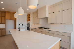 Kitchen featuring an island with sink, decorative light fixtures, light stone counters, recessed lighting, and appliances with stainless steel finishes