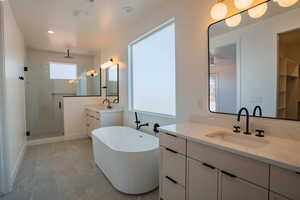 Bathroom featuring a stall shower, two vanities, a soaking tub, and recessed lighting