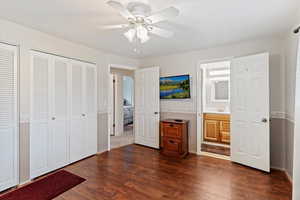 Unfurnished bedroom featuring dark wood-style flooring, connected bathroom, a ceiling fan, and multiple closets