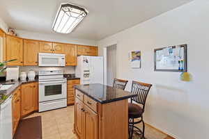 Kitchen featuring white appliances, dark stone countertops, light tile patterned flooring, and a breakfast bar area