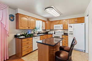 Kitchen with dark stone counters, white appliances, a center island, light tile patterned floors, and a kitchen breakfast bar