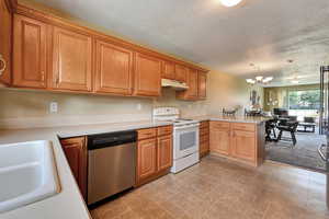 Kitchen with white range with electric stovetop, dishwasher, a peninsula, light countertops, and a textured ceiling