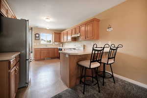 Kitchen with freestanding refrigerator, a breakfast bar area, a peninsula, light countertops, and white electric stove