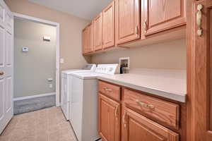 Washroom featuring cabinet space, washer and clothes dryer, and light carpet