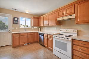 Kitchen featuring electric stove, under cabinet range hood, light countertops, stainless steel dishwasher, and brown cabinets
