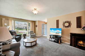 Carpeted living area with a textured ceiling and a warm lit fireplace