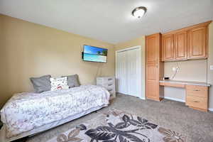 Bedroom with built in desk, light colored carpet, a textured ceiling, and a closet