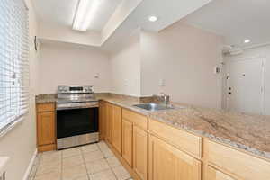 Kitchen with stainless steel range with electric cooktop, light tile patterned floors, light stone countertops, a textured ceiling, and recessed lighting