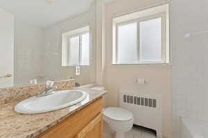 Bathroom with radiator heating unit, vanity, light tile patterned floors, and shower / tub combination