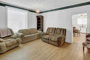 Living area with light wood-style flooring, ornamental molding, and a chandelier
