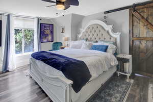 Bedroom with a barn door, wood finished floors, a ceiling fan, and vaulted ceiling