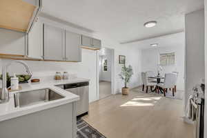 Kitchen with stainless steel appliances, a textured ceiling, light wood-type flooring, gray cabinets, and light stone countertops