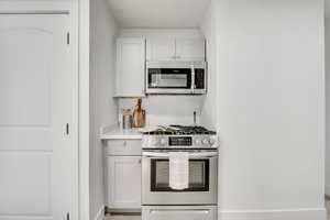 Kitchen with appliances with stainless steel finishes, white cabinetry, and light stone counters